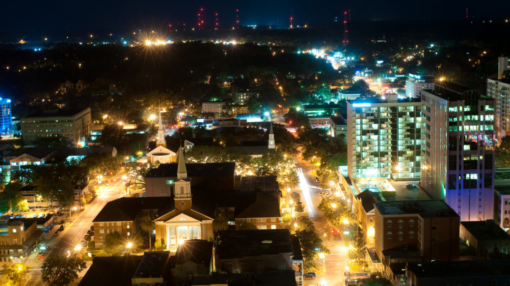 aerial/drone photo of downtown Tallahassee at night, with white, purple and green lights against a black evening sky