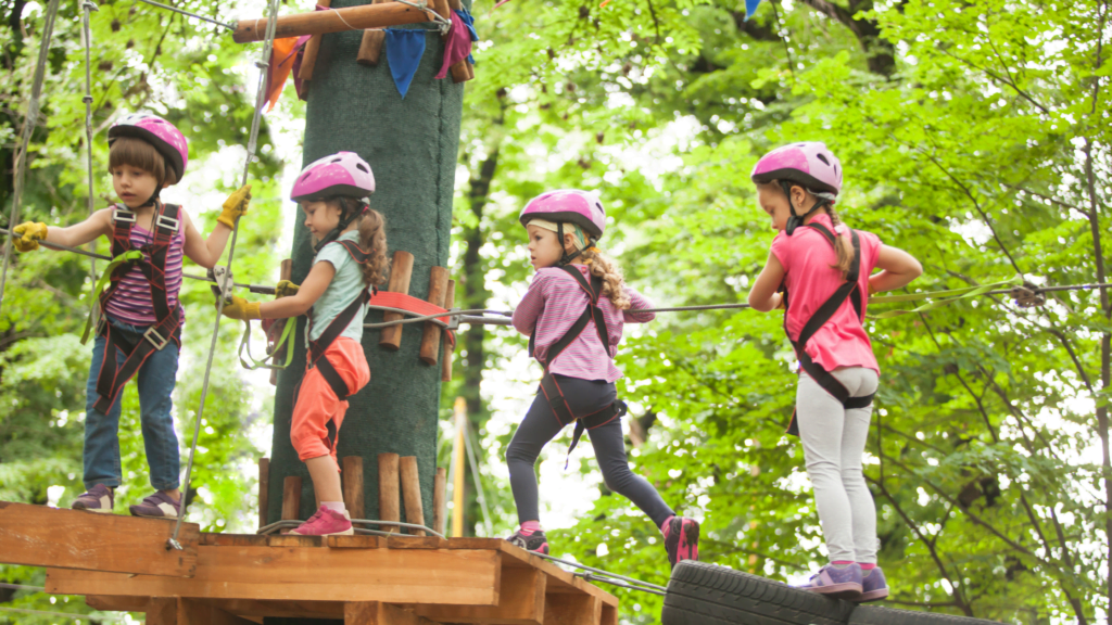 4 children of unknown age, but approximately 8-10 years old, on a tree adventure, complete with helmets and safety gear