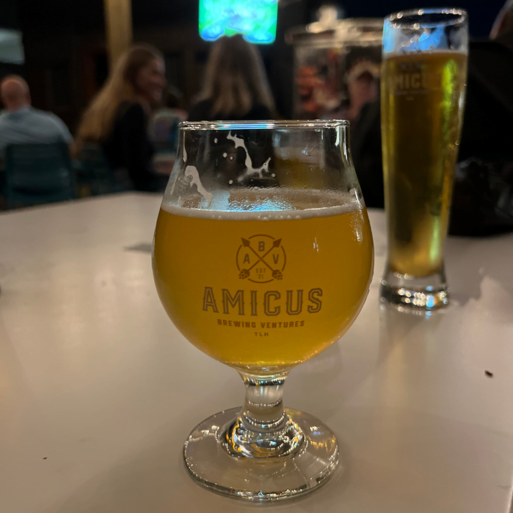 Amicus beer glass on a table at their taphouse, with another beer glass in the background