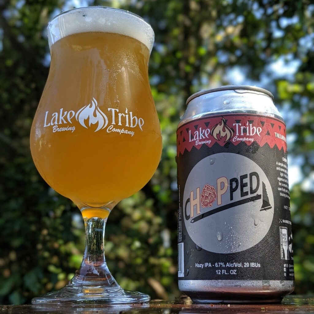 Glass of beer with Lake Tribe logo, next to a bottle of their Chopped beer in a can, with green trees in the background